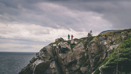 People on cliff by sea against sky