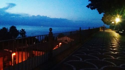 Illuminated railing by sea against sky at night