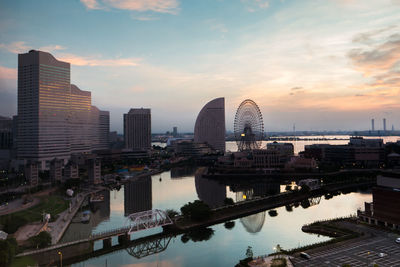 Bridge over river by buildings against sky during sunset