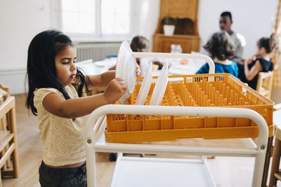 Side view of girl placing plate in crate on cart in classroom