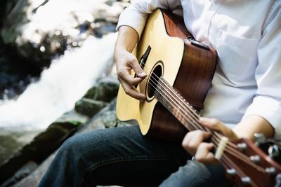 Midsection man playing guitar while sitting by river