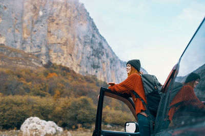 Rear view of young woman sitting on mountain against sky