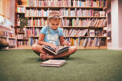 Primary schoolgirl doing homework in school library. student learning from books. back to school