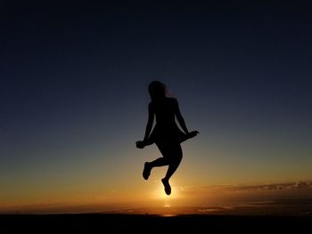 Silhouette man jumping in sea against sky during sunset