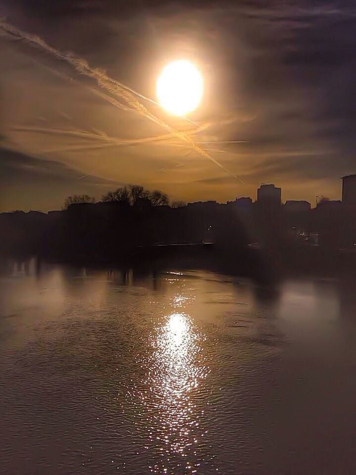 sunset, water, reflection, sun, sky, silhouette, waterfront, architecture, built structure, building exterior, river, scenics, orange color, beauty in nature, lake, cloud - sky, tree, tranquility, tranquil scene, sunlight