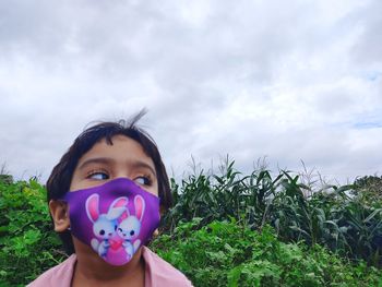 Close-up of girl wearing mask against cloudy sky