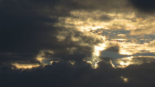 Low angle view of sunlight streaming through clouds