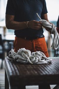 Midsection of man holding rope while standing by table