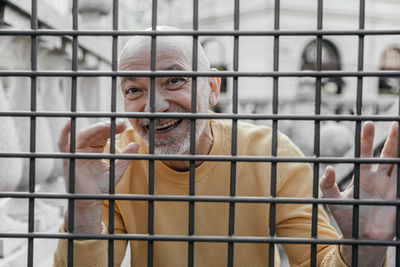 Elderly man showing a vivacious expression while playfully interacting with a metal fence