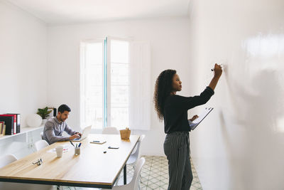 Young businesswoman preparing meeting, writing on wall, colleague working in backgound