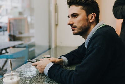 Side view of young businessman sitting by window at cafe