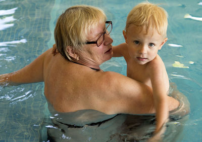Rear view of grandmother with shirtless grandson swimming in pool