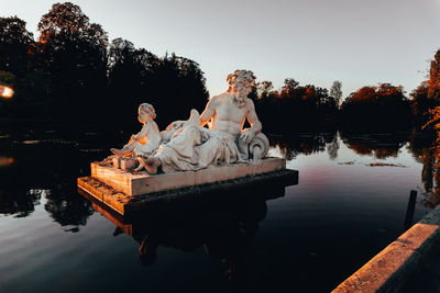Statue amidst lake against clear sky during sunset