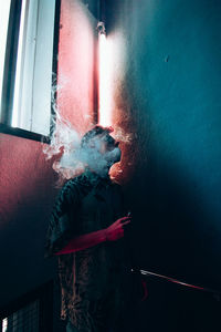 Mature man smoking cigarette while standing against wall at home