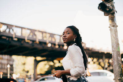 Side view of young woman looking away while standing on street in city