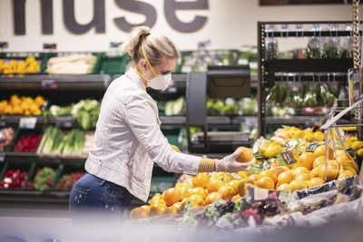 Teenage girl wearing protectice mask and gloves choosing fruits at supermarket