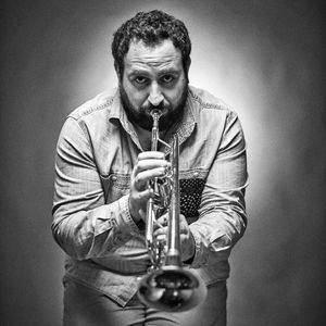 Portrait of man playing trumpet while standing against gray background