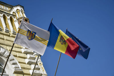 Flags of moldova, european union, city of chisinau are fixed on municipal building against blue sky. 