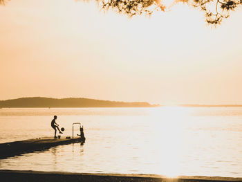 Silhouette people on beach against clear sky during sunset