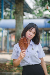 Portrait of young woman holding dried leaf while standing at park