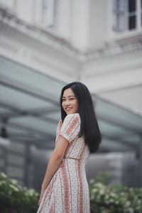 Portrait of smiling young woman standing against built structure