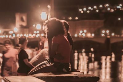 Rear view of friends sitting at illuminated city against sky at night