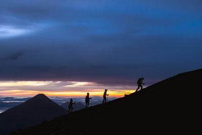 Silhouette people hiking on mountain against cloudy sky during sunset