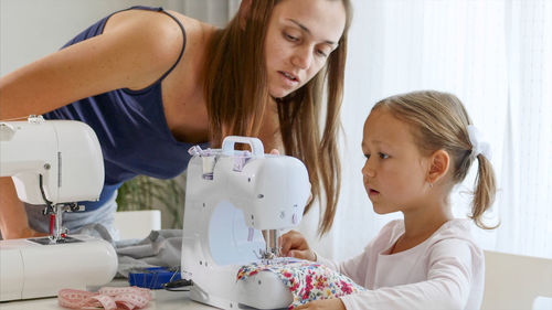 Mother assisting daughter in sewing at home