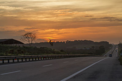 Road by trees against orange sky