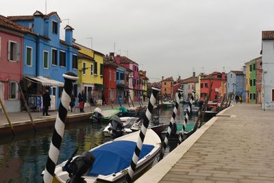 Boats moored on street by buildings against sky