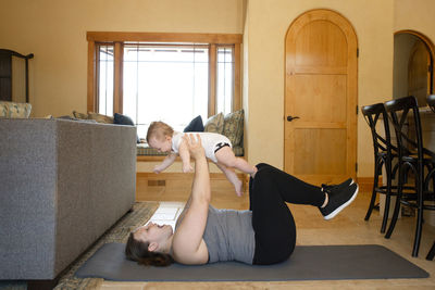 Side view of mother carrying son while exercising on exercise mat at home