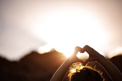 Close-up of boy making heart shape with hands against clear sky