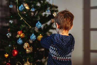 Little cute caucasian boy decorating christmas tree with twinkling decorations.
