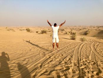 Rear view of man jumping with arms raised on sand at desert 