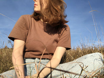 Midsection of woman sitting on field against sky