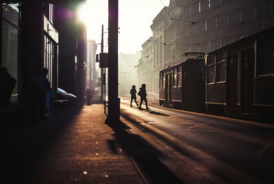 Silhouette women walking by tram on street amidst buildings in city