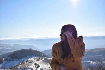 Young woman standing on cliff against mountains during winter