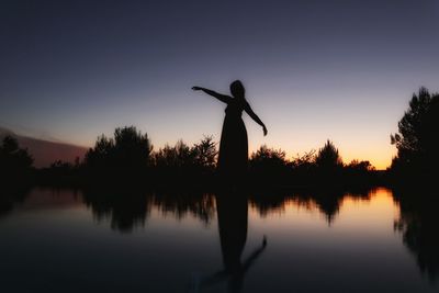 Silhouette woman standing by lake against sky during sunset