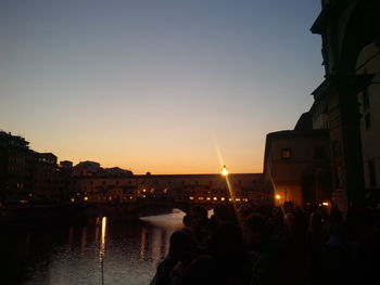 People in city against clear sky during sunset