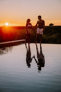 Full length of couple holding hands while standing by infinity pool against sky