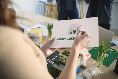 Cropped image of female engineer holding diagrams at table in office