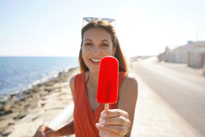 Beautiful young woman offers a popsicle at the camera on summer. focus on popsicle.