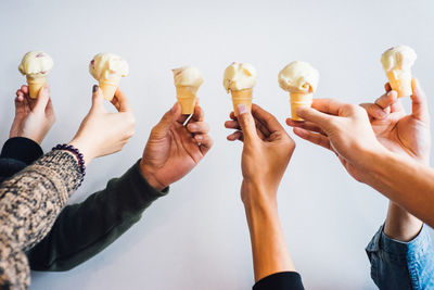 Cropped hands holding ice cream cones over white background