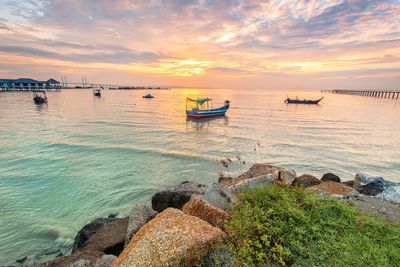 Boats moored on sea against sky during sunset