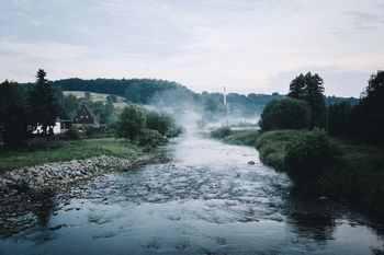 Flowing river against cloudy sky