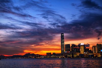 Sea by modern buildings against sky during sunset