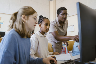 Female teacher explaining students over computer in classroom at school