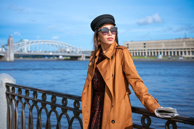 Young woman wearing sunglasses standing against bridge