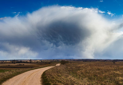 Dirt road amidst field against sky