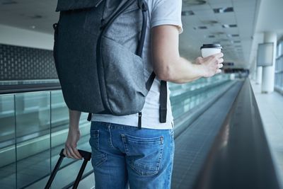 Man walking with suitcase. rear view of traveler on moving walkway at airport terminal.